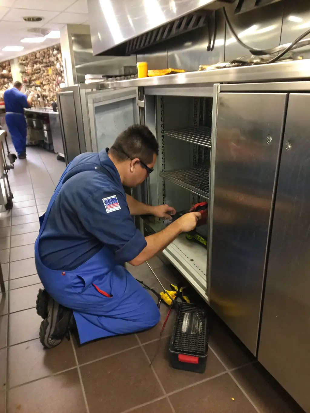 A technician is shown repairing a Viking freezer in a commercial kitchen, with frozen goods neatly organized in the background. This image represents our Viking Freezer Repair service.